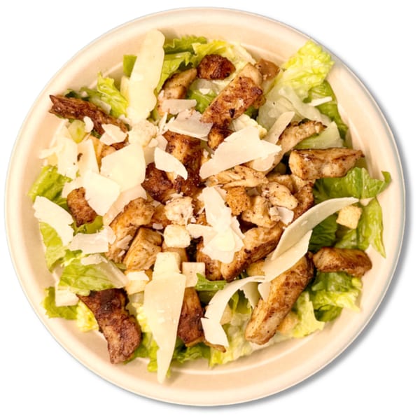 Caesar salad with grilled chicken, parmesan shavings, and croutons in a light-colored bowl.
